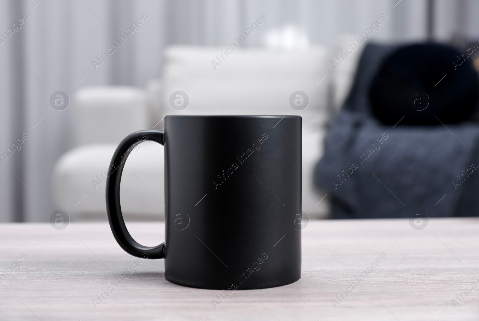 Photo of One blank black ceramic mug on white wooden table. Mockup for design