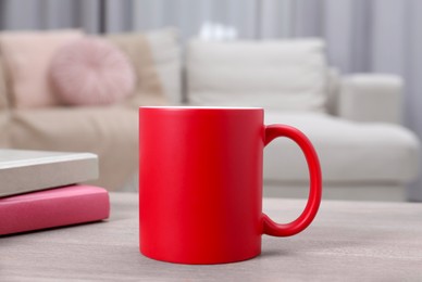 Photo of Blank red ceramic mug and notebooks on wooden table. Mockup for design