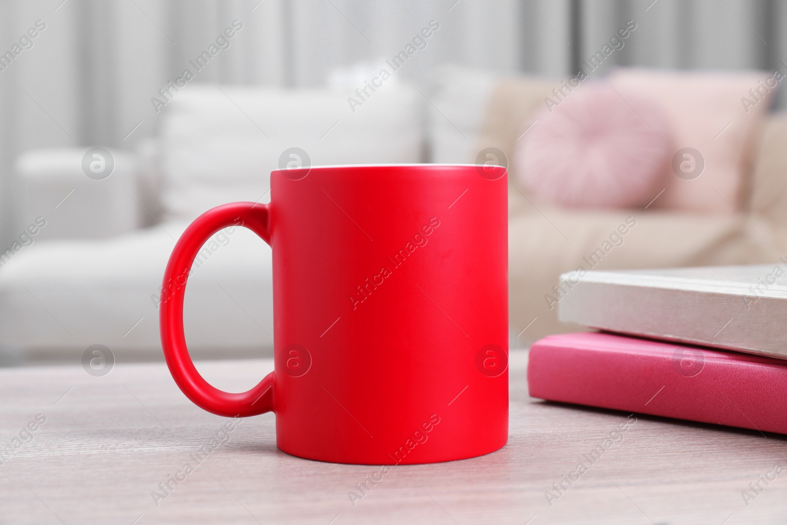 Photo of Blank red ceramic mug and notebooks on wooden table. Mockup for design