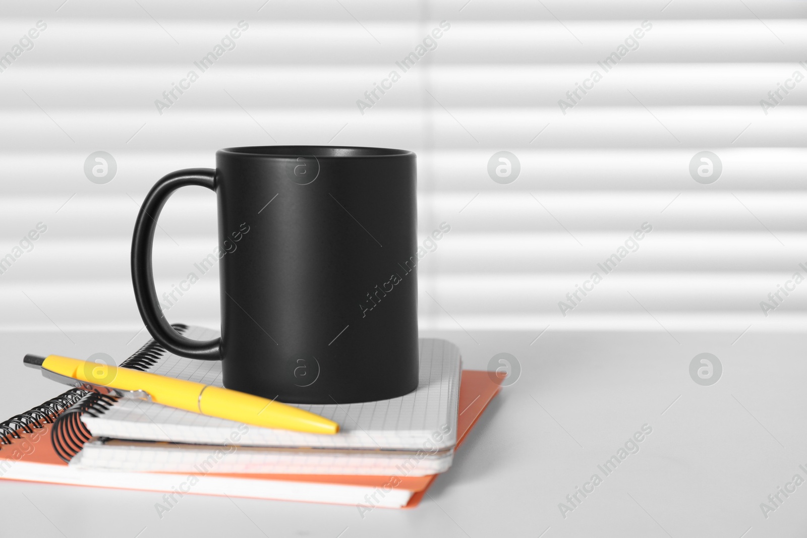 Photo of One blank black ceramic mug and stationery on white table. Mockup for design