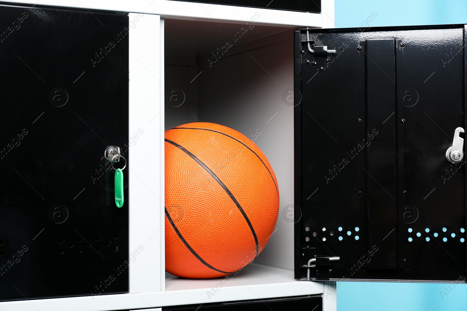 Photo of Open locker with basketball ball on light blue background, closeup