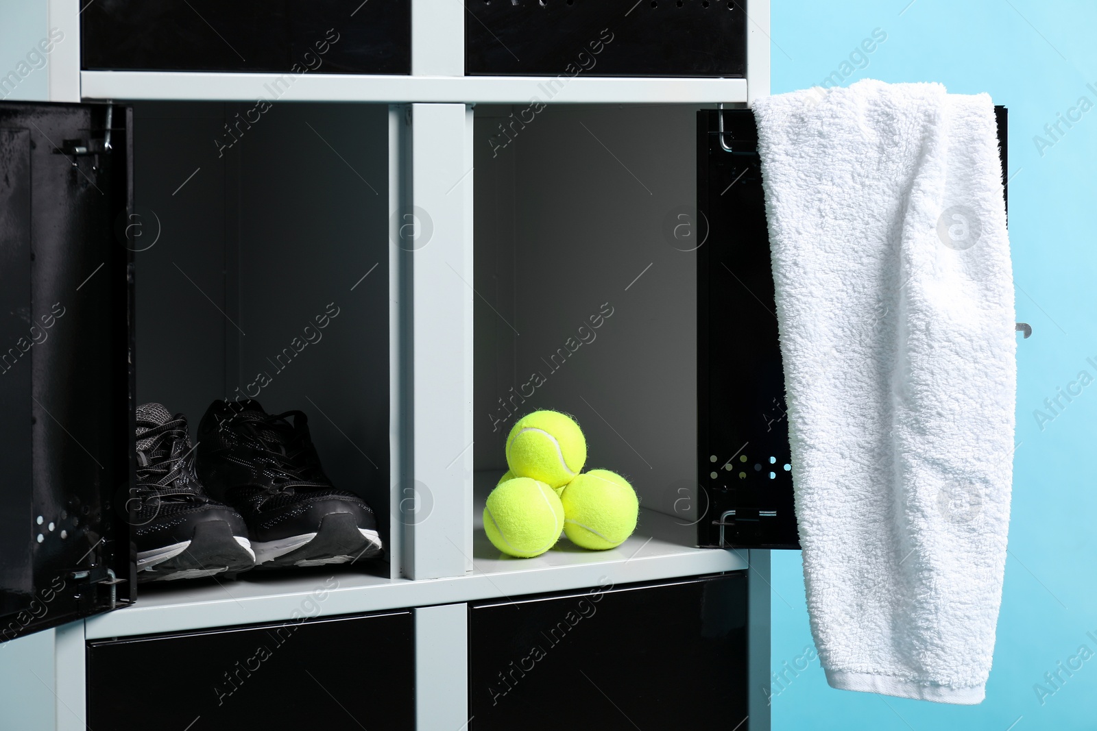 Photo of Open lockers with tennis balls, sneakers and towel on light blue background