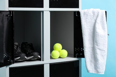 Photo of Open lockers with tennis balls, sneakers and towel on light blue background