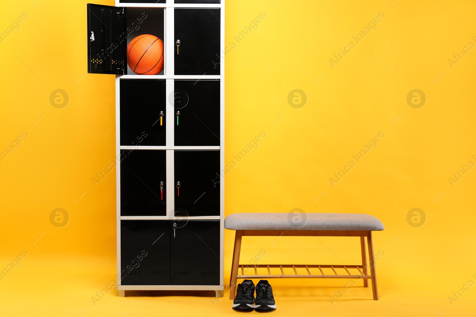 Photo of Open locker with basketball ball, bench and sneakers on orange background