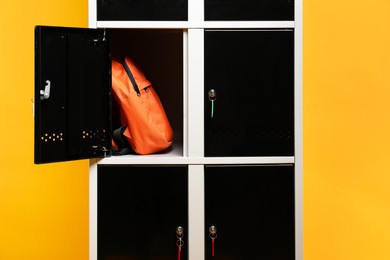 Photo of Open locker with backpack on orange background