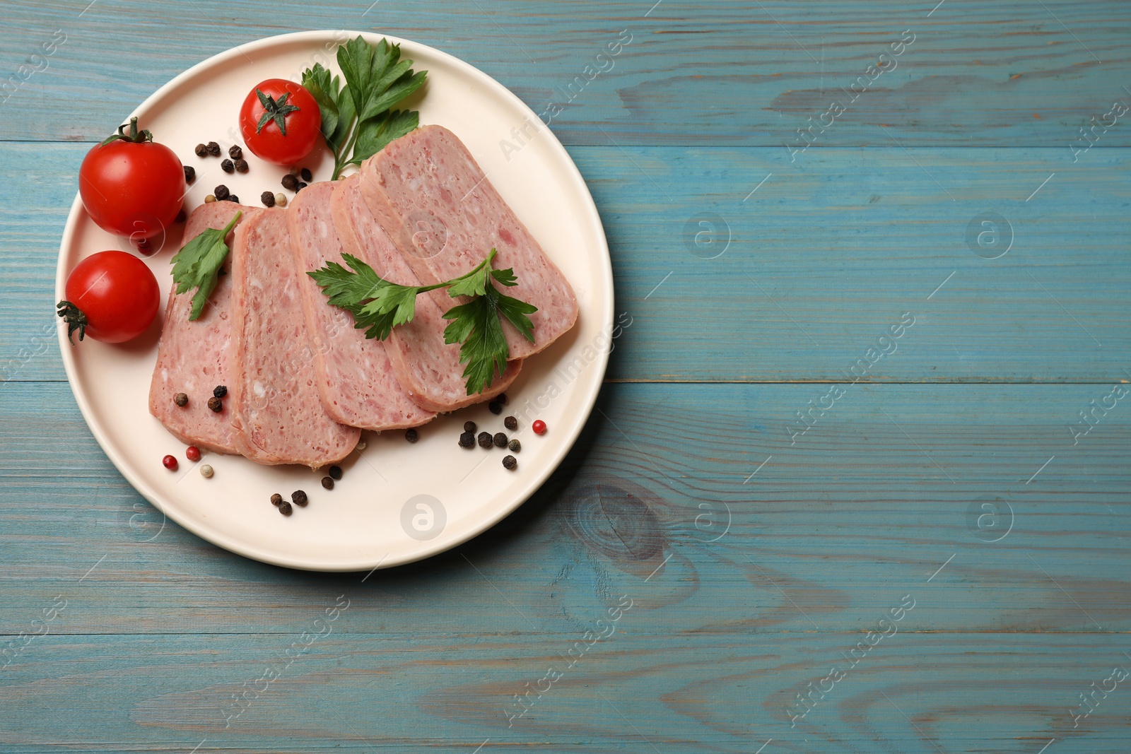 Photo of Pieces of tasty canned meat, parsley, peppercorns and tomatoes on light blue wooden table, top view. Space for text