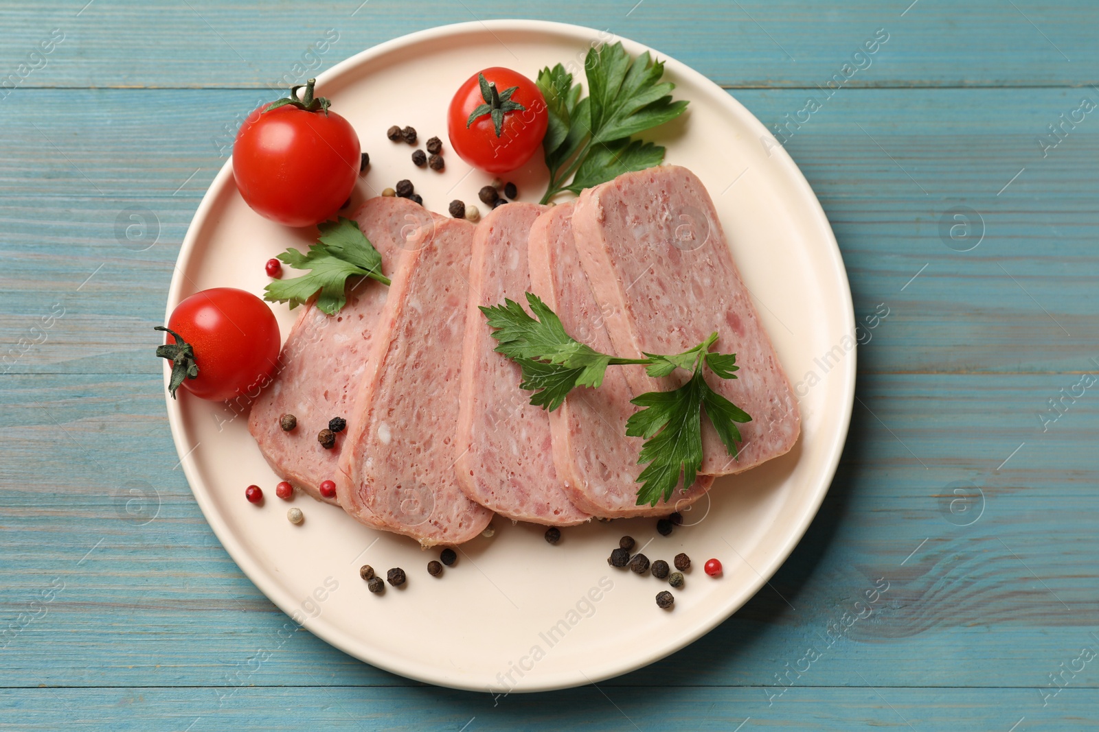 Photo of Pieces of tasty canned meat, parsley, peppercorns and tomatoes on light blue wooden table, top view