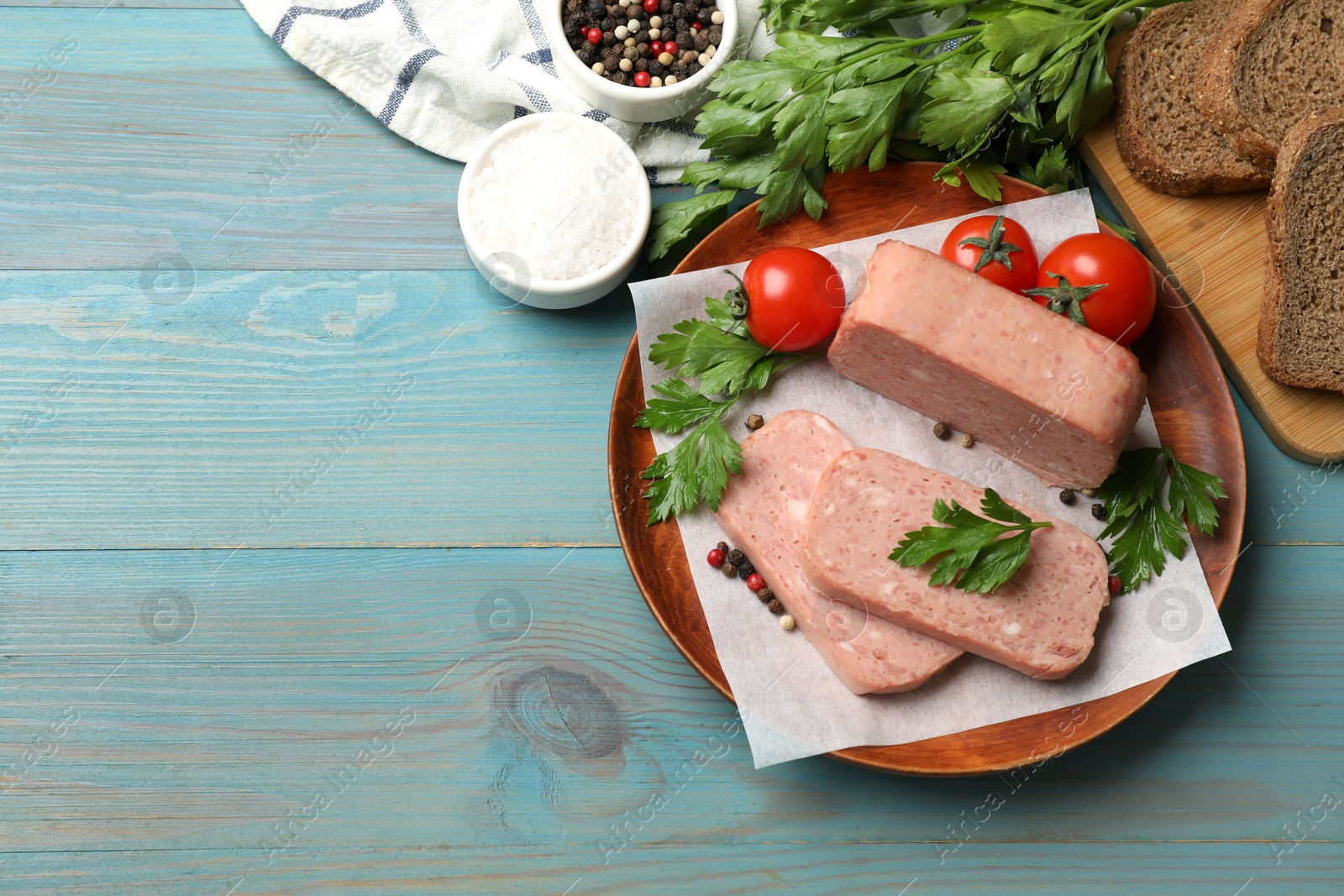 Photo of Pieces of tasty canned meat, parsley, spices and tomatoes on light blue wooden table, flat lay. Space for text