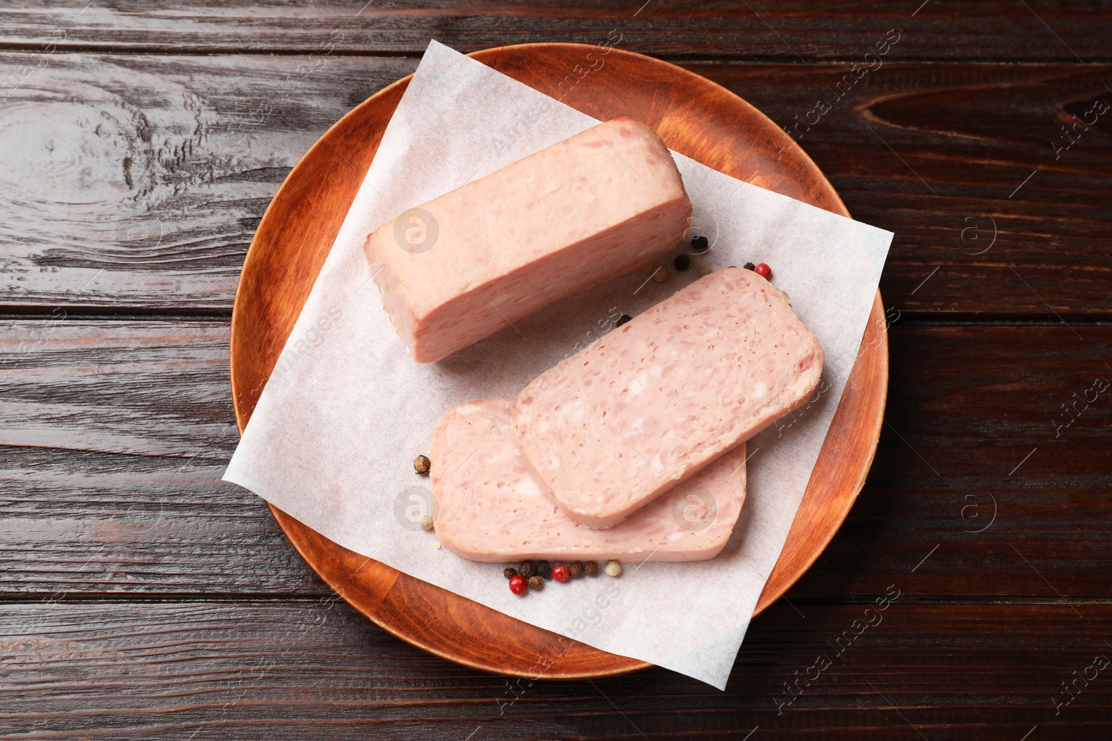 Photo of Pieces of tasty canned meat and peppercorns on wooden table, top view