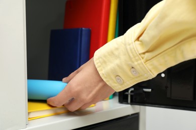 Photo of Woman putting school supplies into locker, closeup