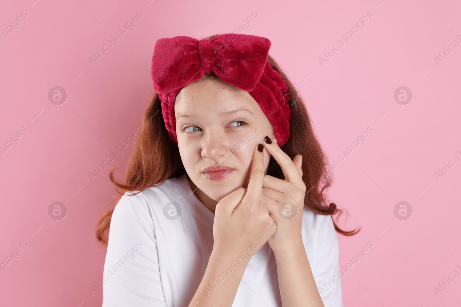 Photo of Teenage girl popping pimple on her face against pink background. Acne problem