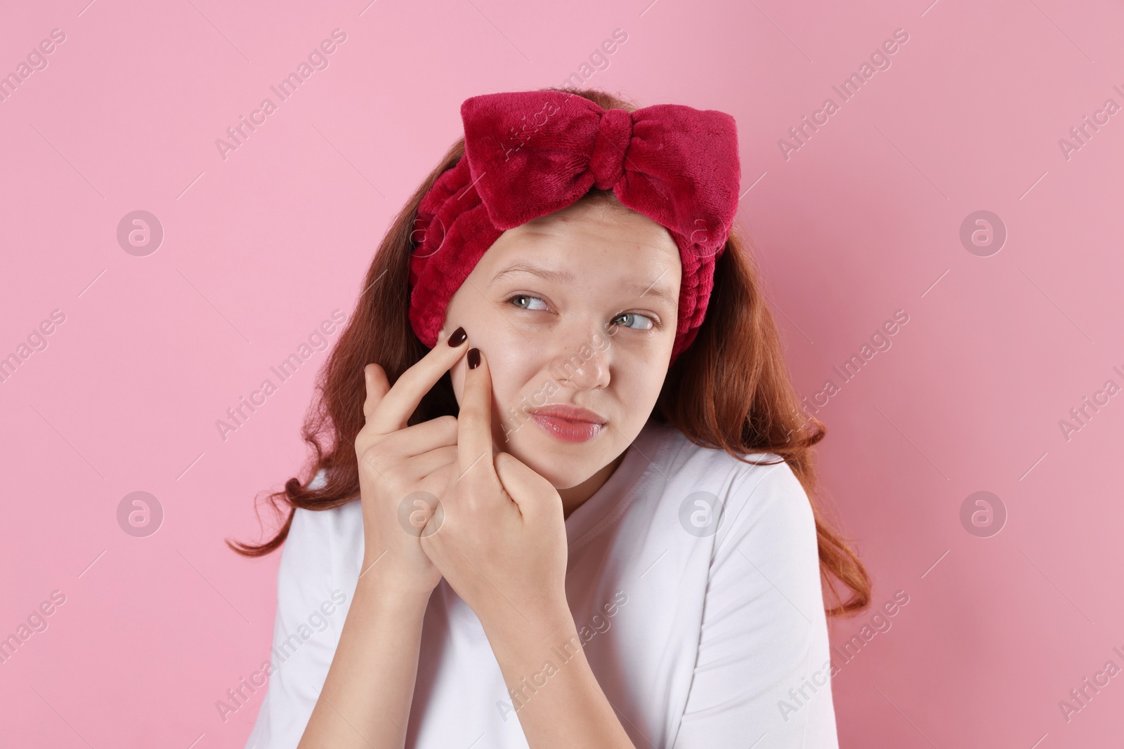 Photo of Teenage girl popping pimple on her face against pink background. Acne problem