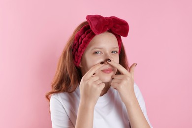 Photo of Teenage girl popping pimple on her face against pink background. Acne problem