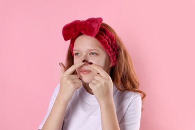 Photo of Teenage girl popping pimple on her face against pink background. Acne problem