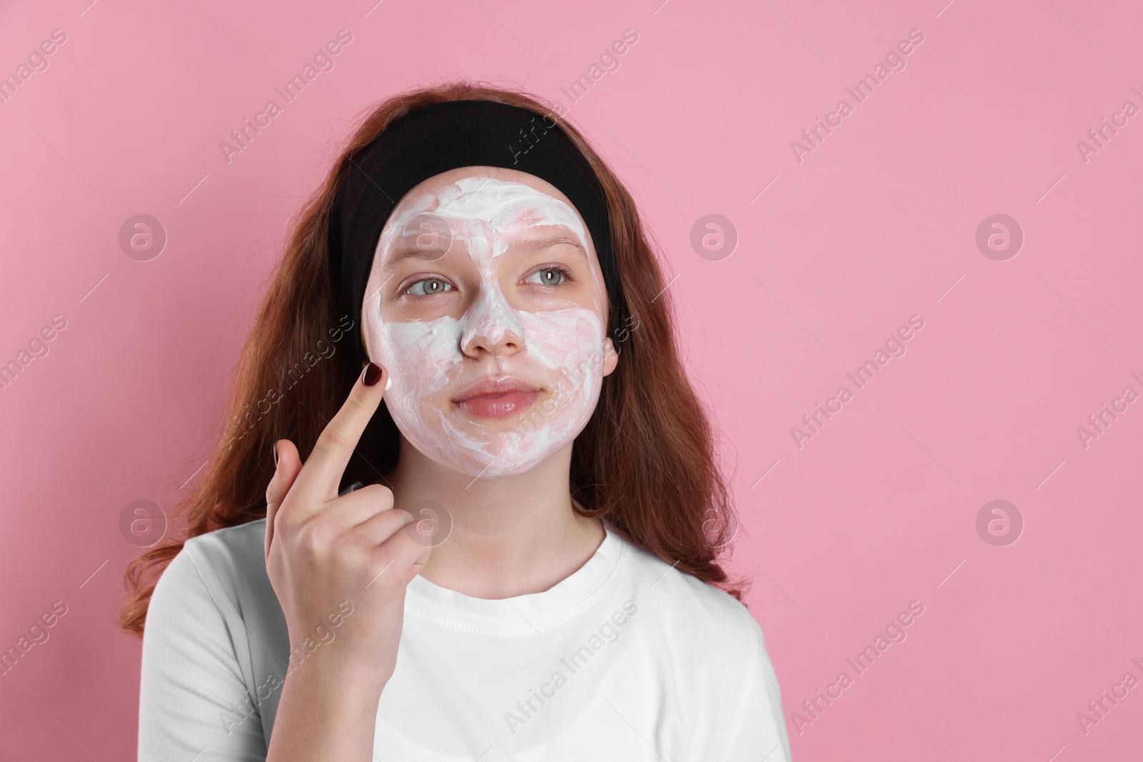 Photo of Teenage girl applying mask on her face with against pink background, space for text. Cosmetic product