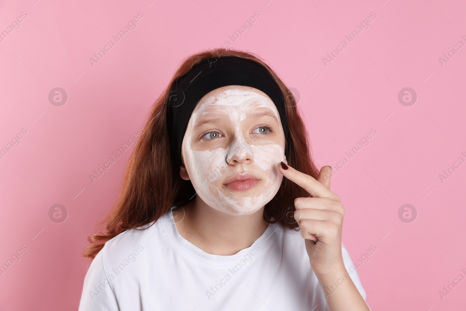 Photo of Teenage girl applying mask on her face with against pink background. Cosmetic product