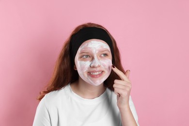 Photo of Teenage girl applying mask on her face with against pink background. Cosmetic product