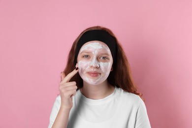 Photo of Teenage girl applying mask on her face with against pink background. Cosmetic product