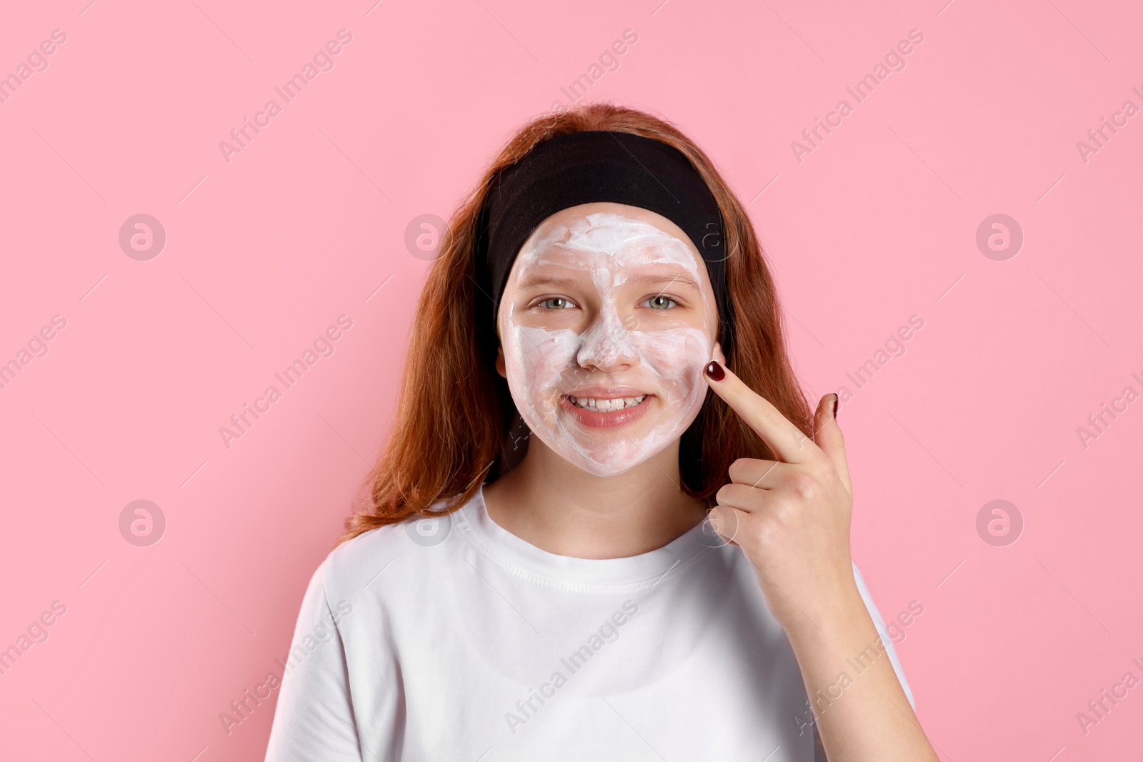 Photo of Teenage girl applying mask on her face with against pink background. Cosmetic product