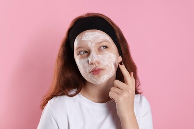 Photo of Teenage girl applying mask on her face with against pink background. Cosmetic product