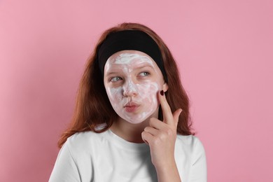 Photo of Teenage girl applying mask on her face with against pink background. Cosmetic product