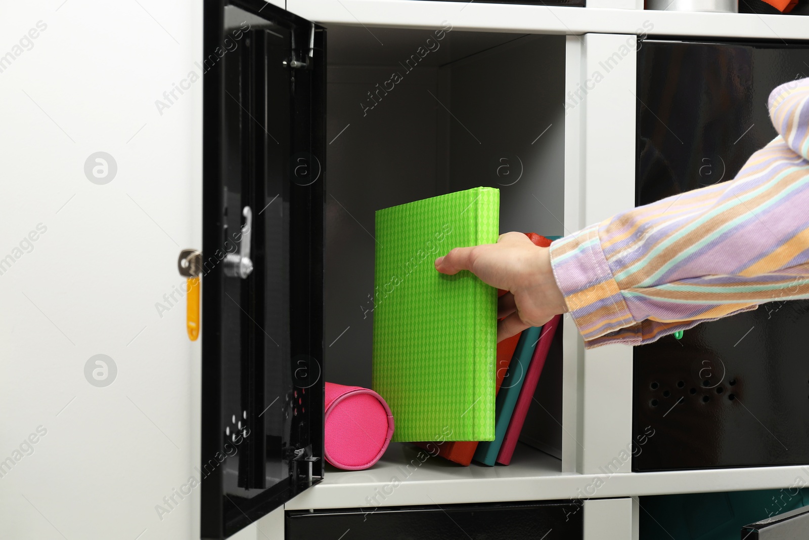 Photo of Woman putting book into locker indoors, closeup