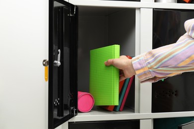 Photo of Woman putting book into locker indoors, closeup