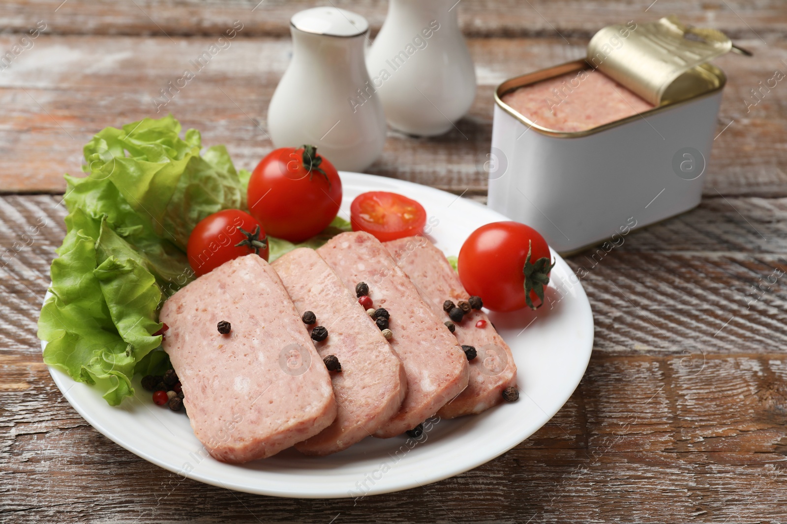 Photo of Tasty canned meat, tomatoes, lettuce and spices on wooden table, closeup