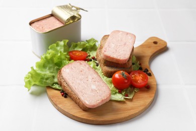 Photo of Tasty canned meat, bread, tomatoes, spices and lettuce on white tiled table