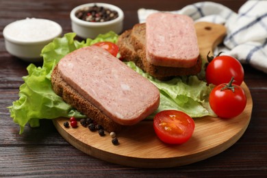 Tasty canned meat, bread, tomatoes, spices and lettuce on wooden table, closeup