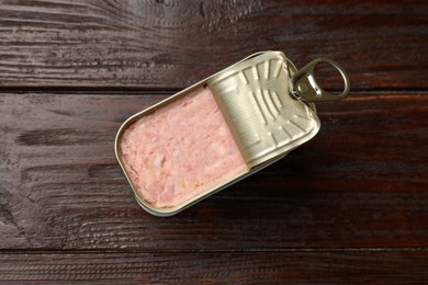 Photo of Tasty canned meat in tin can on wooden table, top view