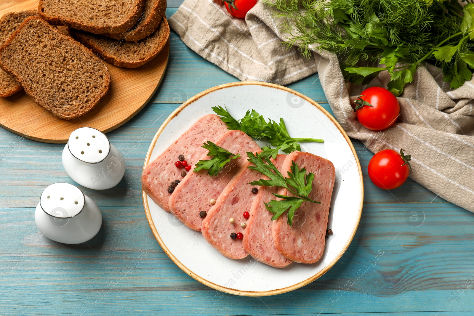 Photo of Tasty canned meat, spices, bread and tomatoes on light blue wooden table, flat lay