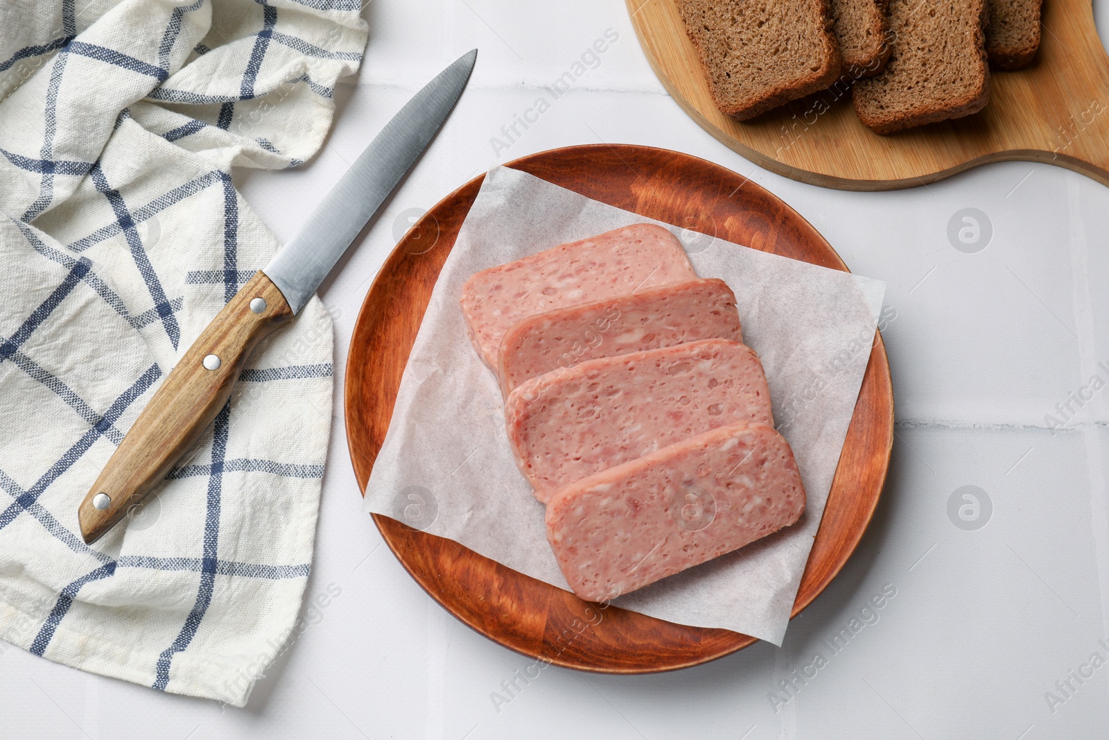 Photo of Canned meat, knife and bread on white tiled table, flat lay