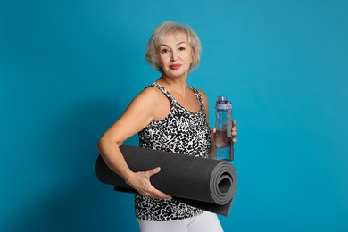 Photo of Senior woman with fitness mat and water on light blue background, space for text