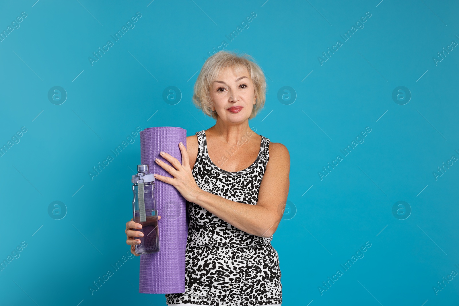 Photo of Senior woman with fitness mat and water on light blue background