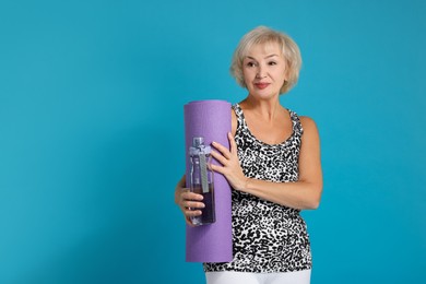 Photo of Senior woman with fitness mat and water on light blue background, space for text