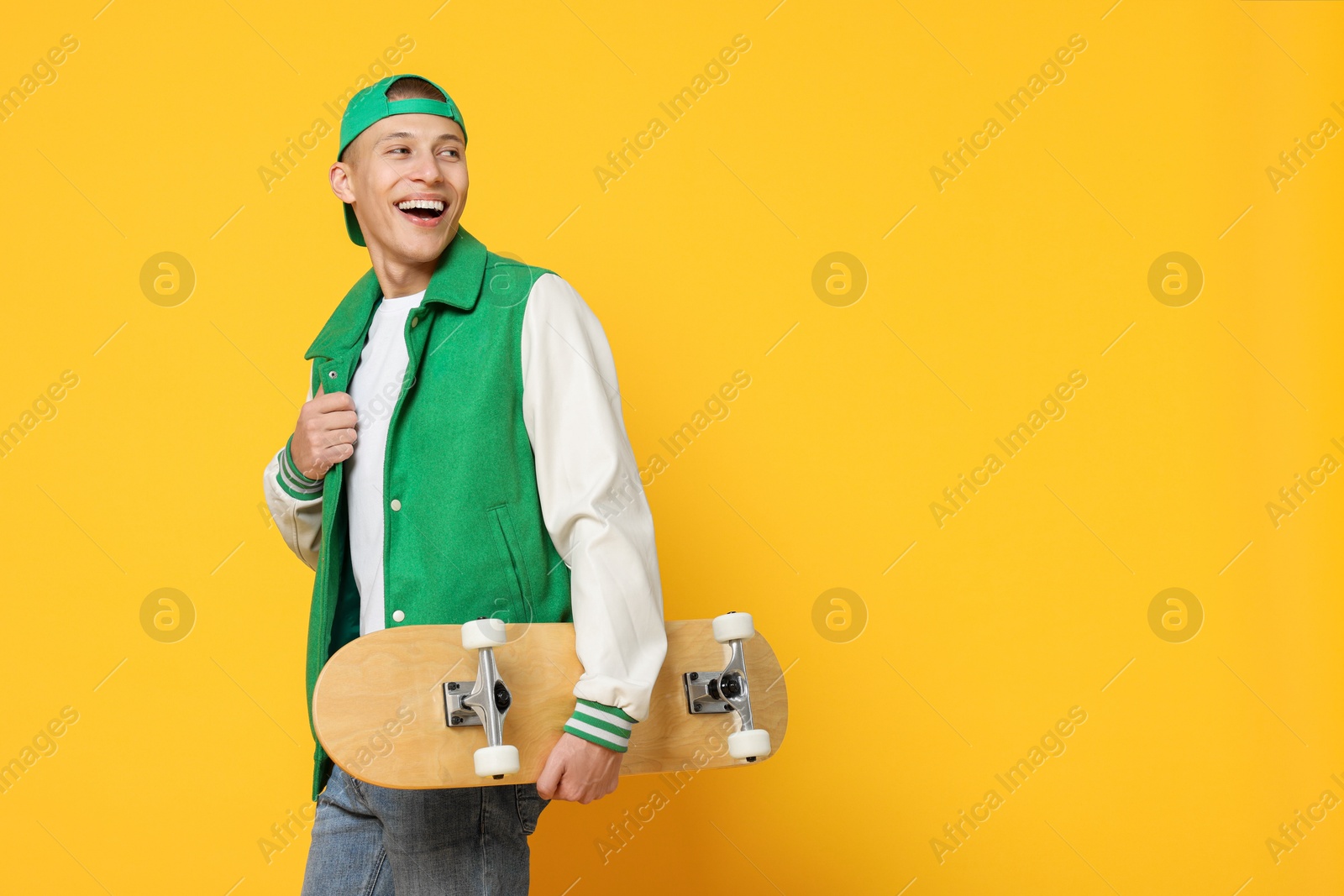 Photo of Happy man with skateboard on orange background. Space for text