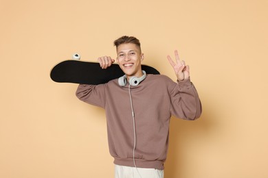 Photo of Happy man with skateboard and headphones showing peace sign on beige background