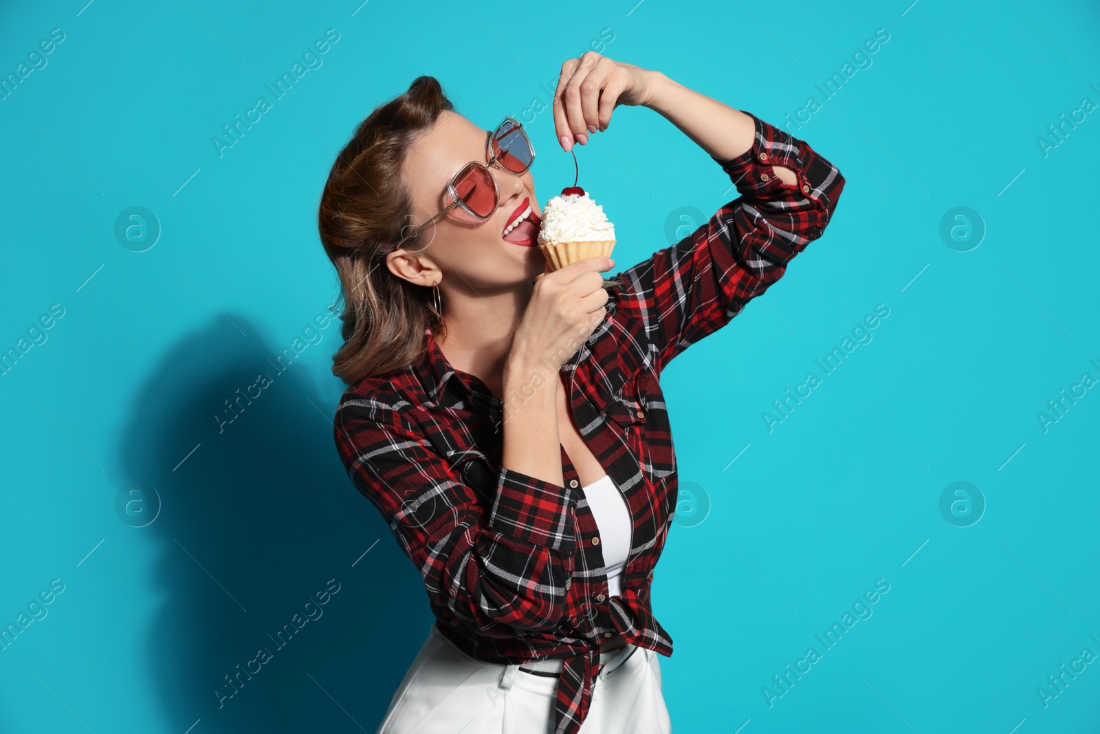 Photo of Attractive pin-up woman eating cupcake on light blue background