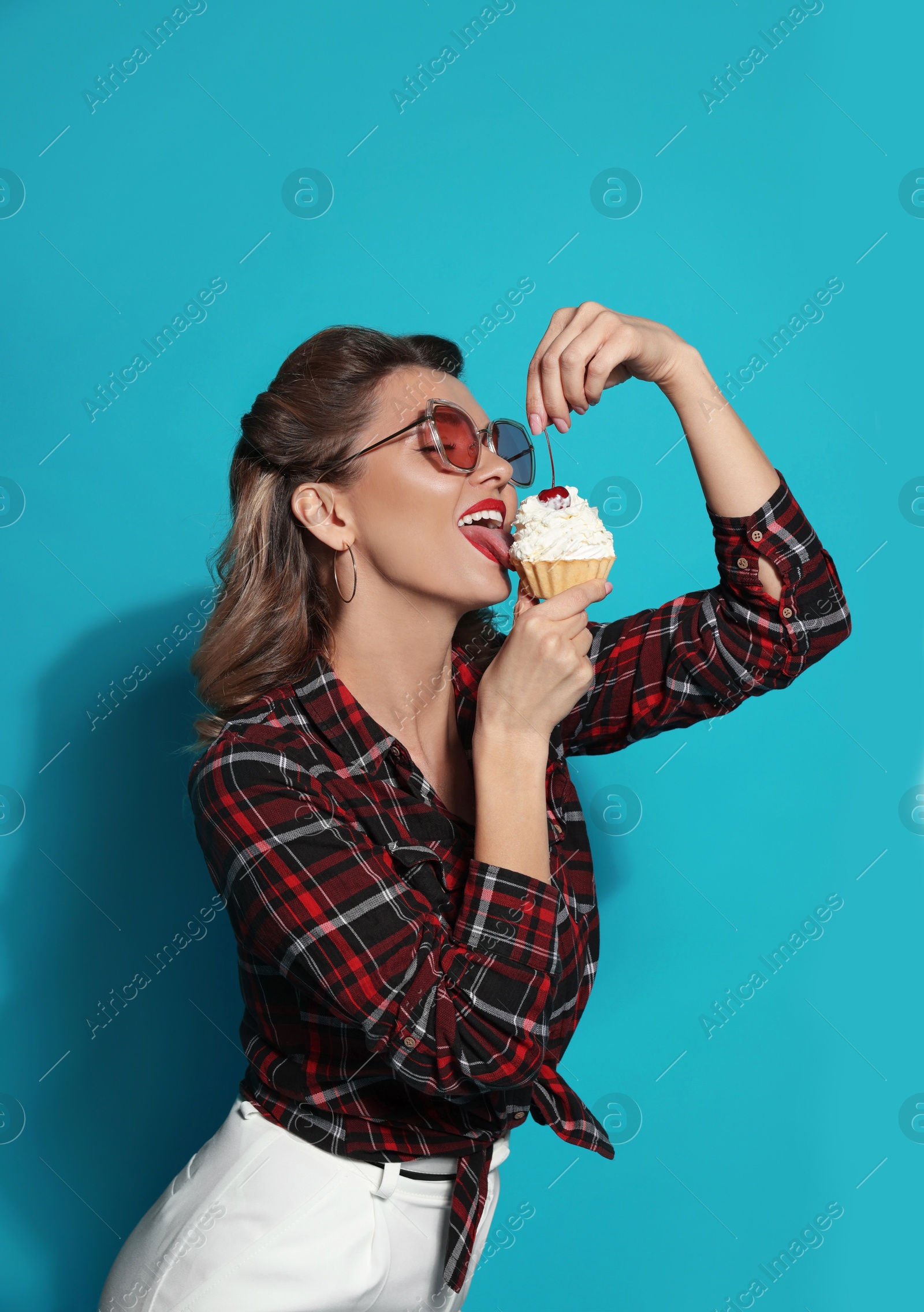 Photo of Attractive pin-up woman eating cupcake on light blue background