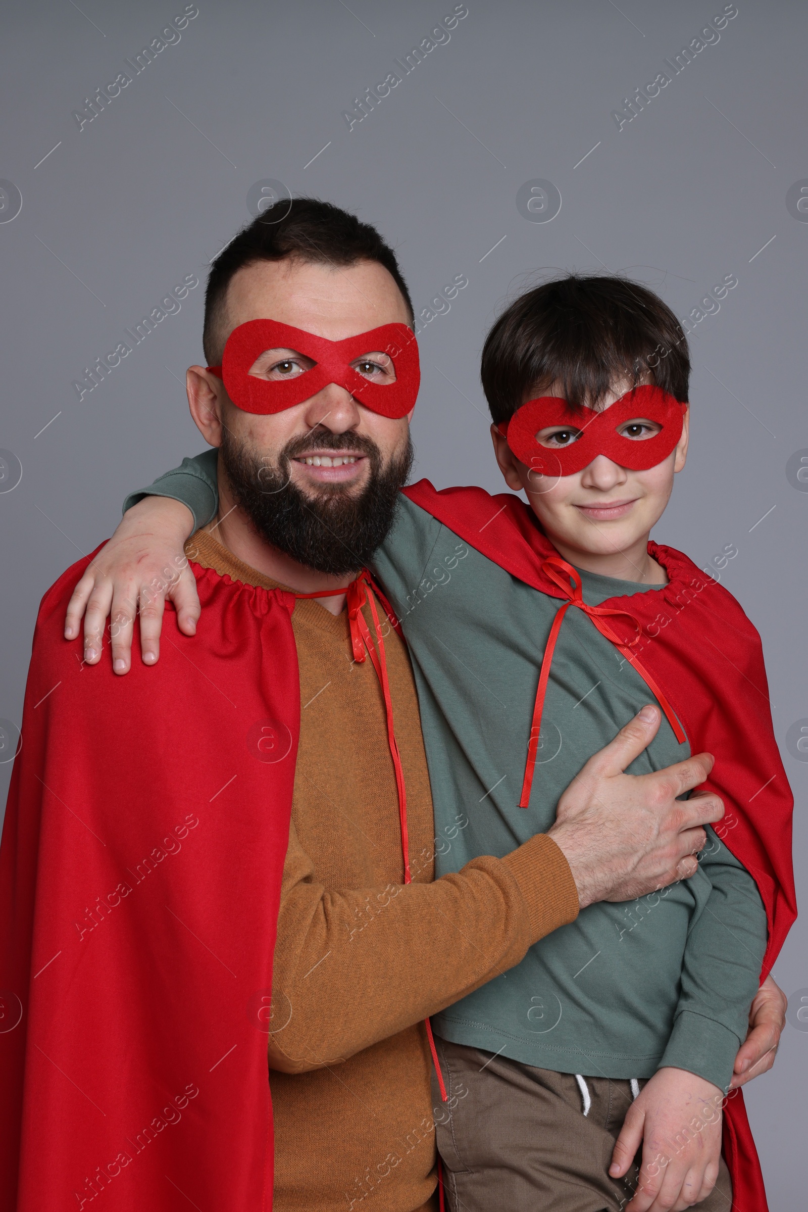 Photo of Father and his son wearing superhero costumes on gray background