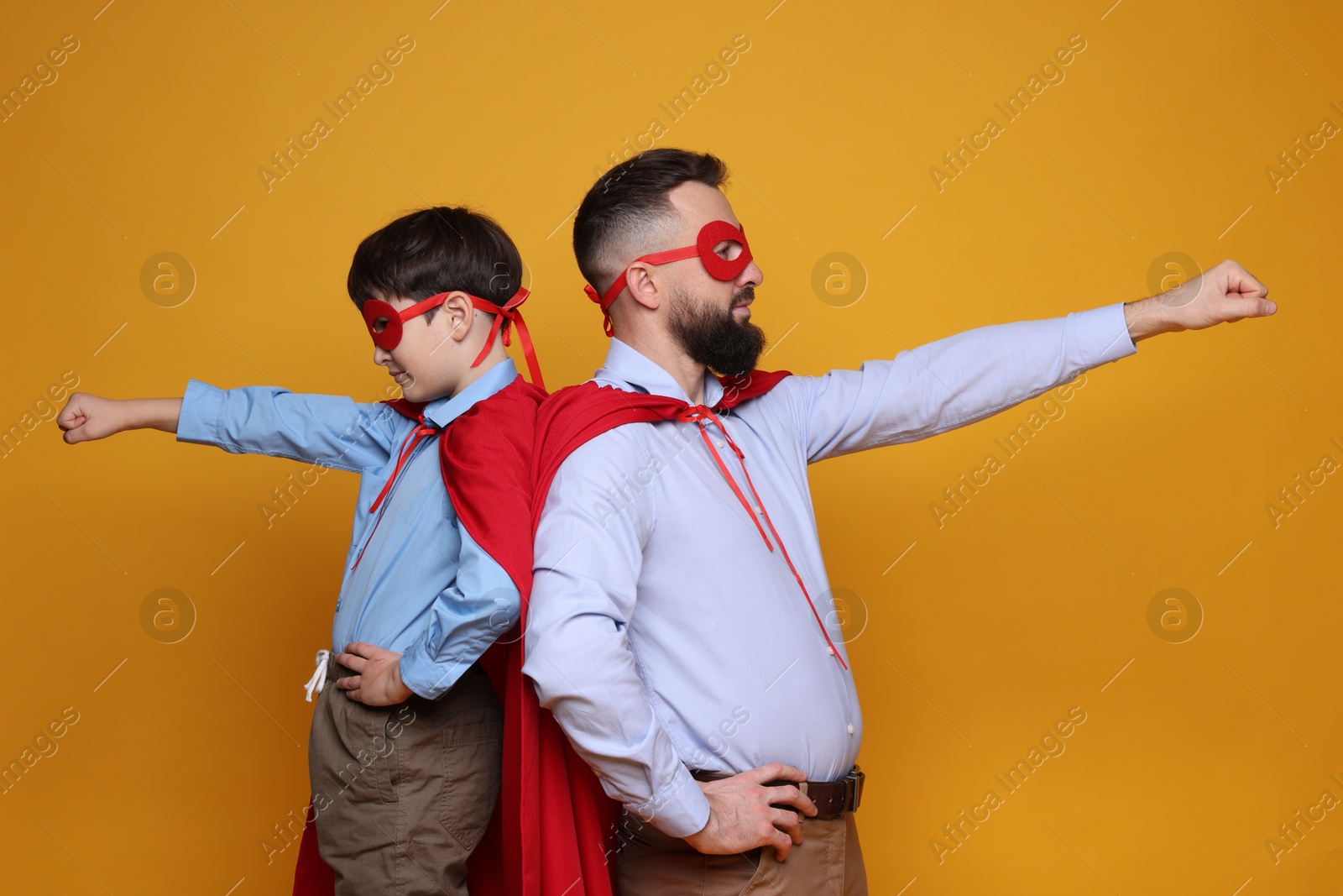 Photo of Father and his son wearing superhero costumes on orange background