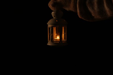 Photo of Woman holding Christmas lantern with burning candle in darkness, closeup. Space for text