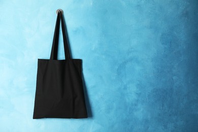 Photo of Black eco bag hanging on light blue wall. Mockup for design