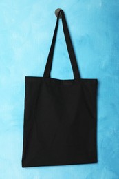 Photo of Black eco bag hanging on light blue wall. Mockup for design