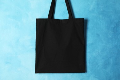 Photo of Black eco bag hanging on light blue wall. Mockup for design