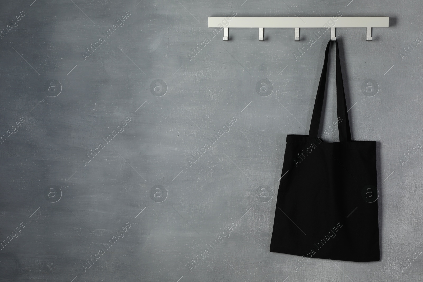 Photo of Black eco bag hanging on grey wall. Mockup for design