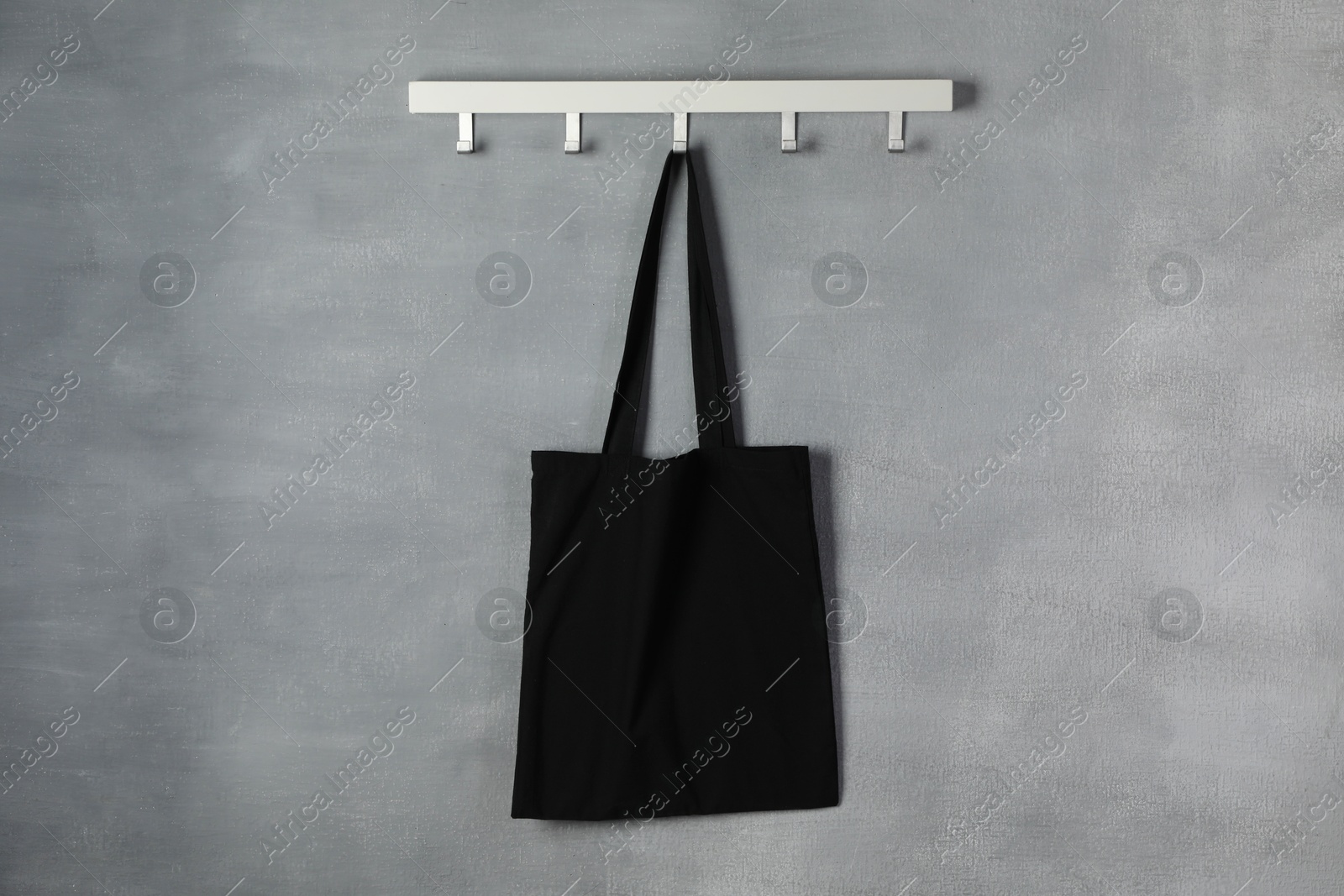 Photo of Black eco bag hanging on grey wall. Mockup for design