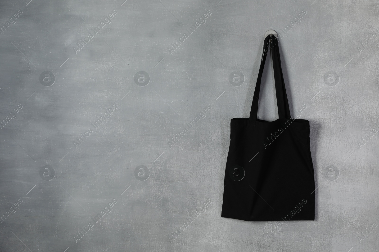 Photo of Black eco bag hanging on grey wall. Mockup for design