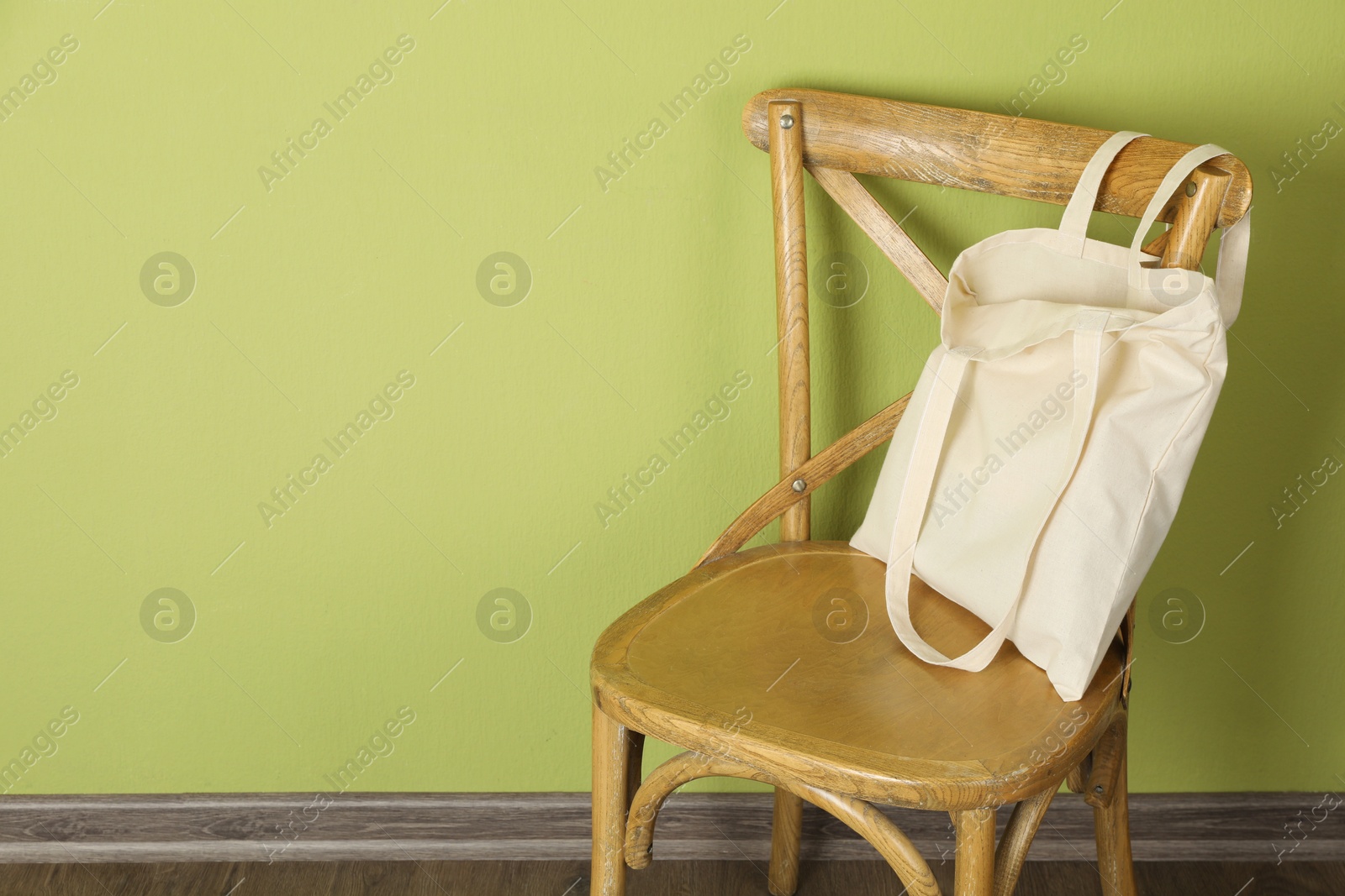 Photo of One eco bag on wooden chair near green wall. Mockup for design